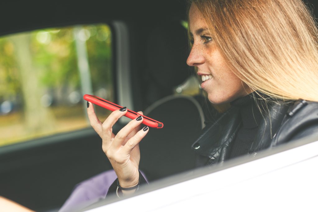 Jak włączyć autokorektę w telefonie? Słownik i podpowiadanie słów Dziewczyna siedząca w samochodzie używająca smartfona uśmiechnięta nastolatka rozmawiająca z przyjaciółką młoda kobieta ciesząca się wolnym czasem